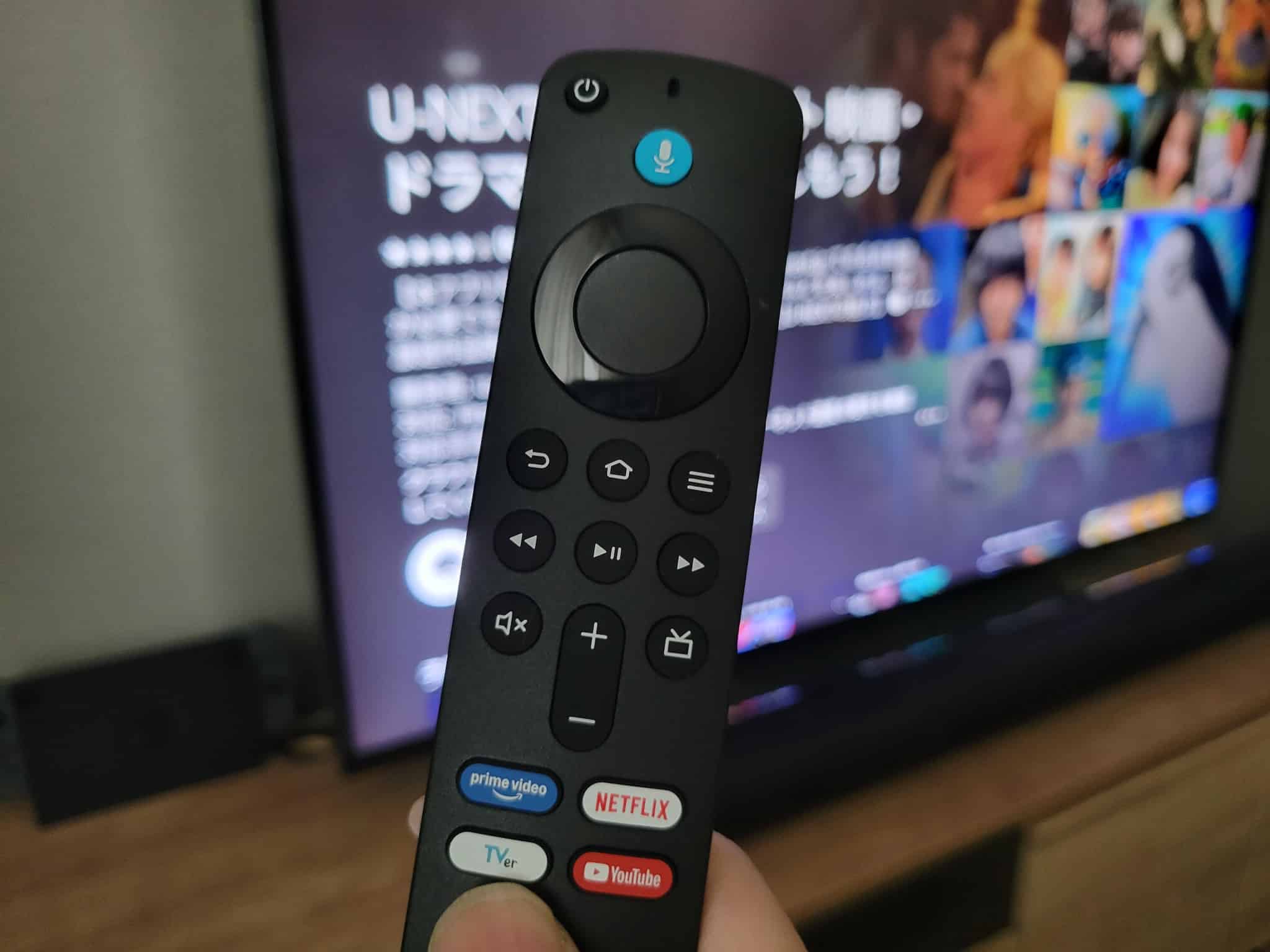 U-NEXTを表示したテレビの前でFire TV Stick 4K Selectのリモコンを持っている様子